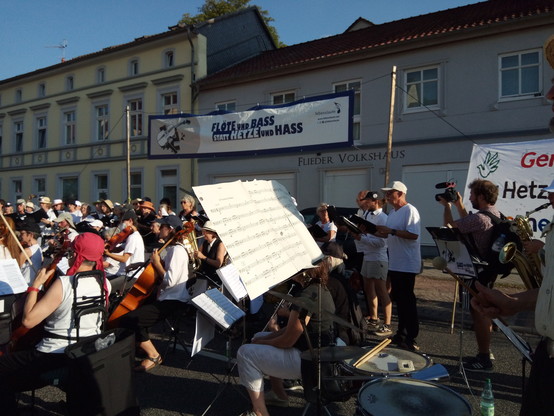 schräges Foto über das Lebenslaute-Ensemble hinweg, es ist zu sehen dass sie mit dem Rücken zu einem Haus mit der Aufschrift 