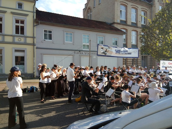 Auf der Straße vor ein paar Wohnhäusern hat sich das Lebenslaute-Orchester + Chor aufgestellt und spielt auf